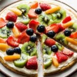 Delicious dessert pizza topped with fresh fruits like strawberries, blueberries, and kiwi.